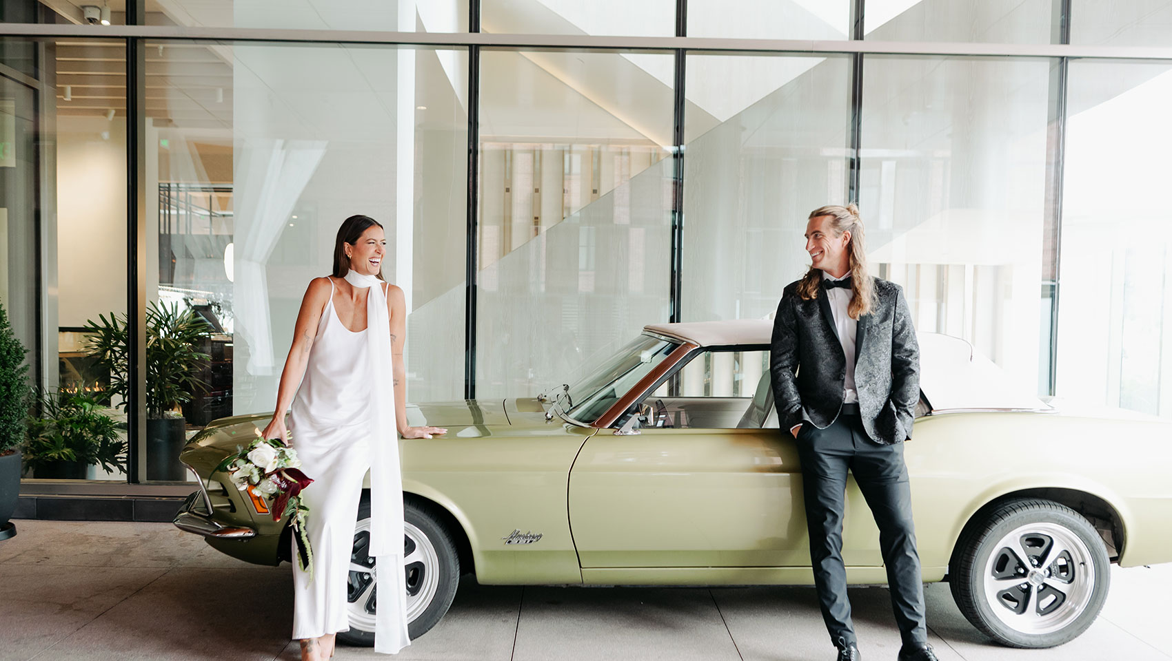 Bride and Groom stand in front of vintage convertible at Kimpton Claret Hotel