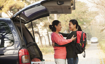 Mother and daughter hug behind trunk of car