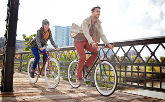 Man and woman ride bikes across a bridge
